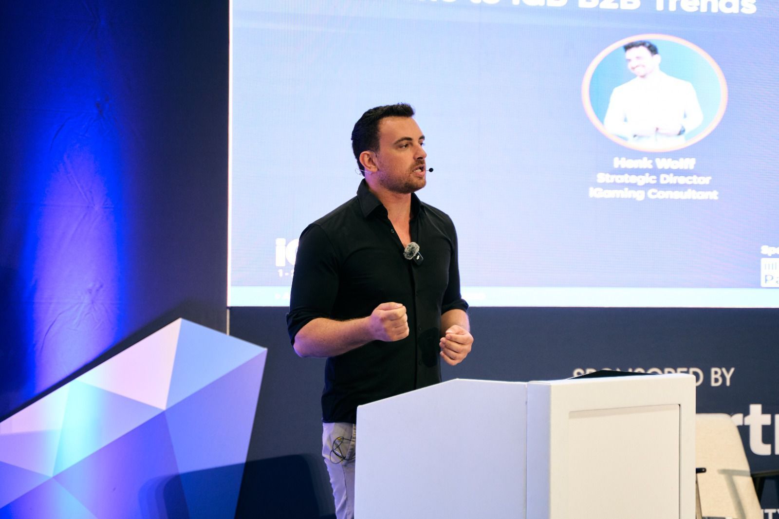 Henk Wolff mid-gesture during his iGB B2B Trends keynote, headset microphone on and his speaker slide behind him.