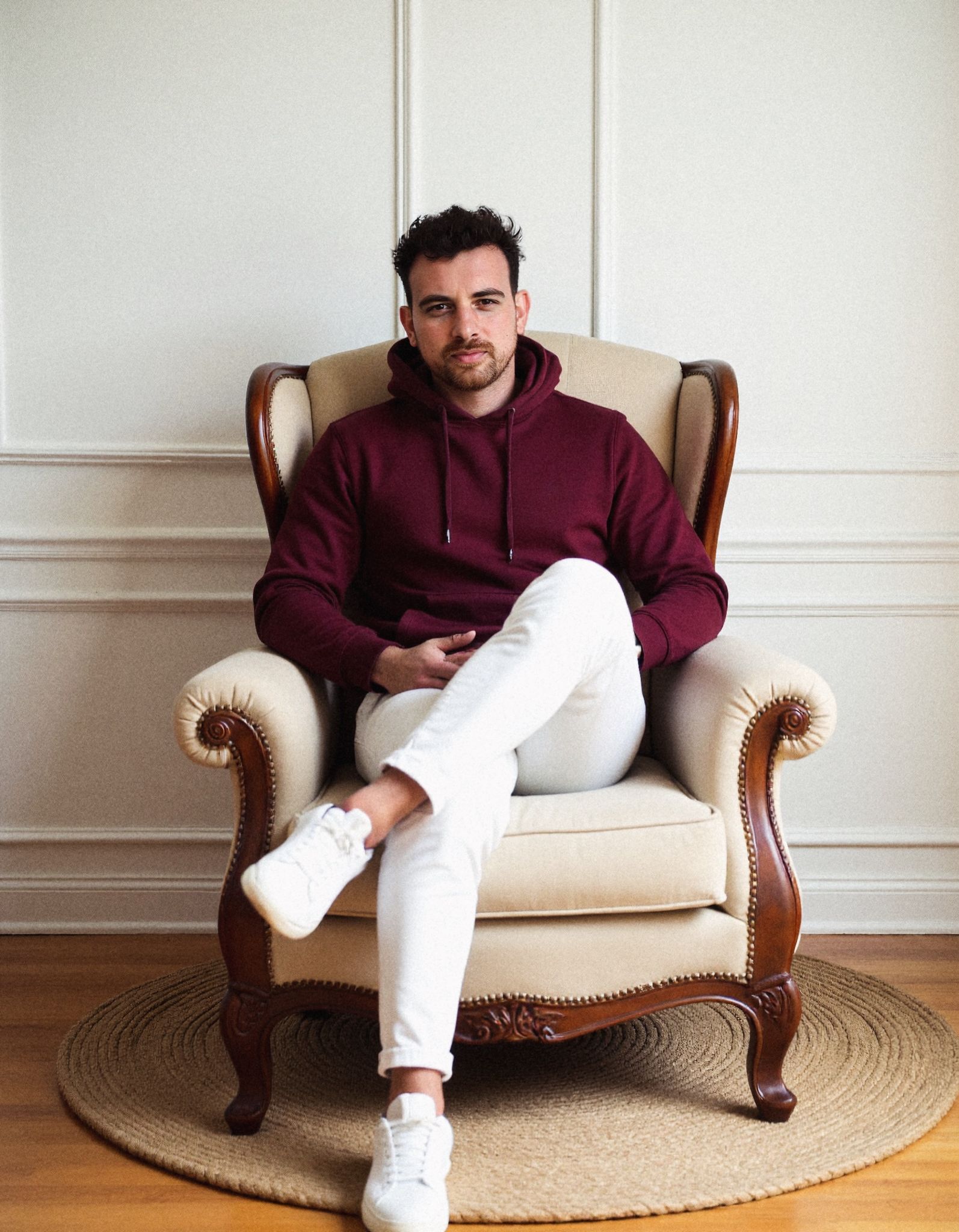 Wide portrait of Henk Wolff seated in a cream wingback armchair on a round jute rug in a panelled room.