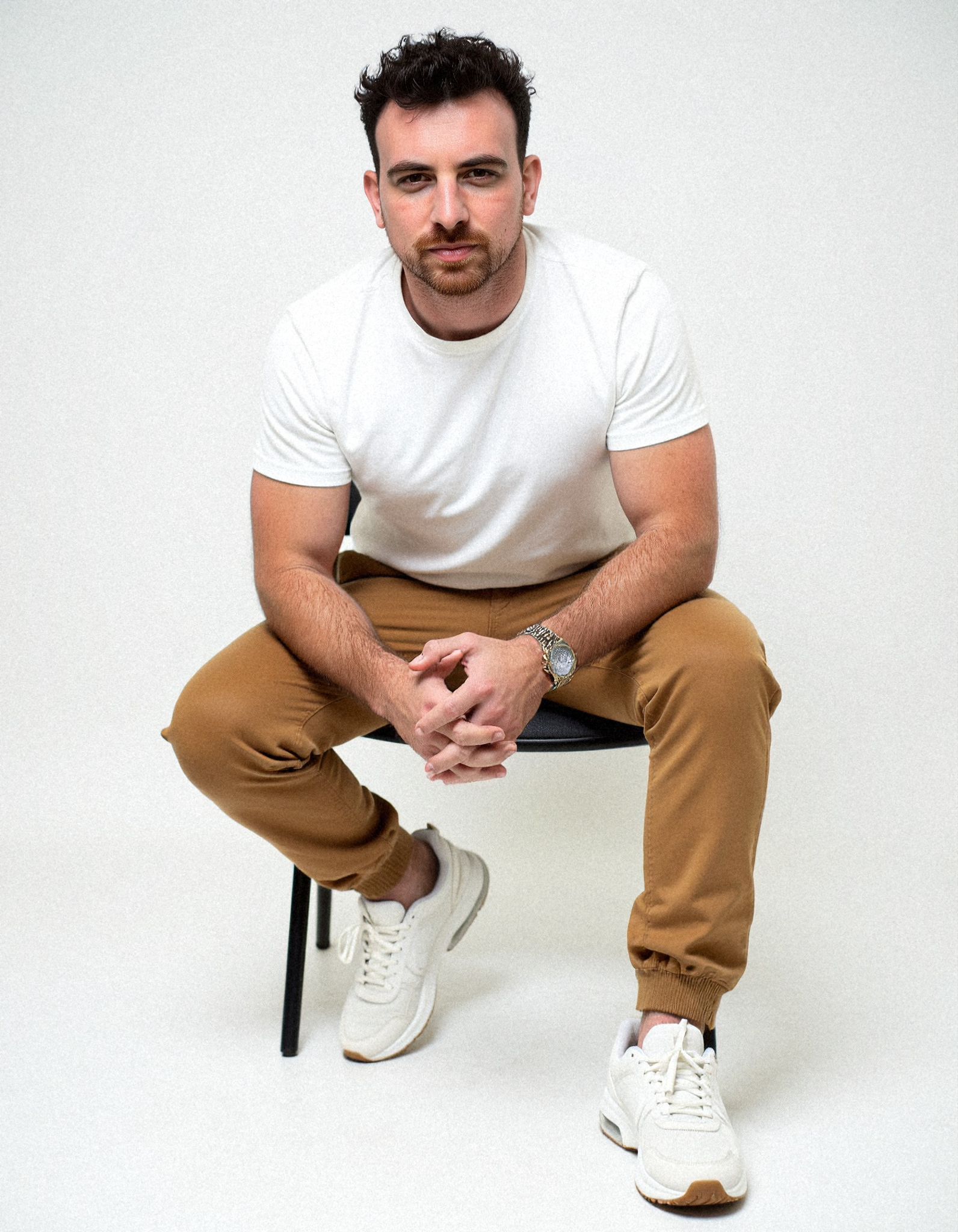 Studio portrait of Henk Wolff seated on a stool against a plain white backdrop, hands clasped in front of him.